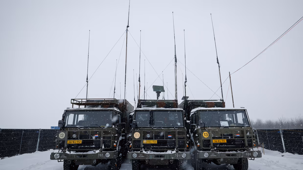 Drie legervrachtwagens van voren gezien. Erboven steken lange antennes uit.