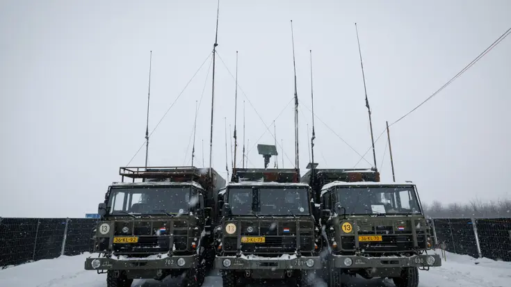 Drie legervrachtwagens van voren gezien. Erboven steken lange antennes uit.