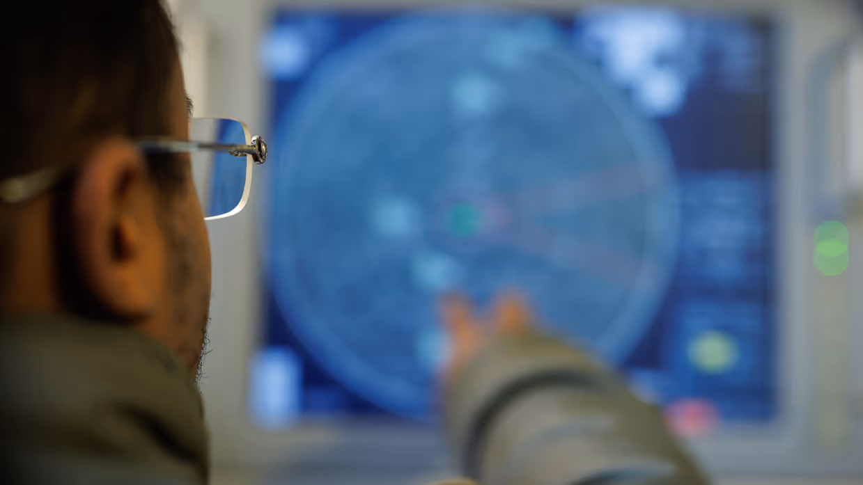 Een collega kijkt naar een blauw radarscherm met geblurde informatie.