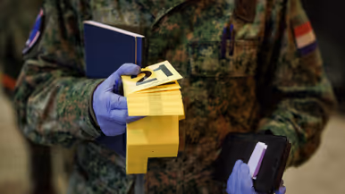 Links zet Rick een geel bordje op de grond met daarop het cijfer acht neer bij een rood tasje. Rick draagt blauwe hopesjes om zijn schoenen. Op de rechterfoto draagt Rick gele, genummerde bordjes en een boekje. Hij heeft blauwe, plastic handschoentjes aan.
