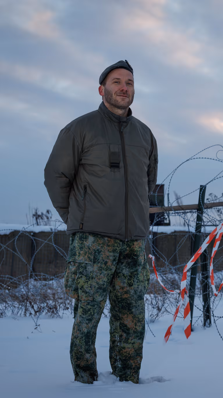 Portretfoto van Leon in besneeuwd landschap. Op de achtergrond staat de lanceerinrichting van het Patriot-wapensysteem. 