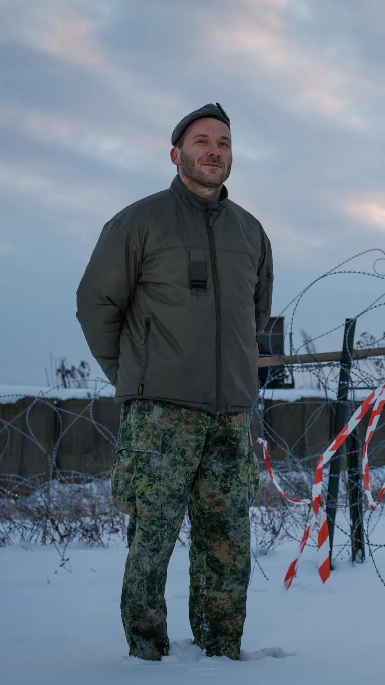 Portretfoto van Leon in besneeuwd landschap. Op de achtergrond staat de lanceerinrichting van het Patriot-wapensysteem. 
