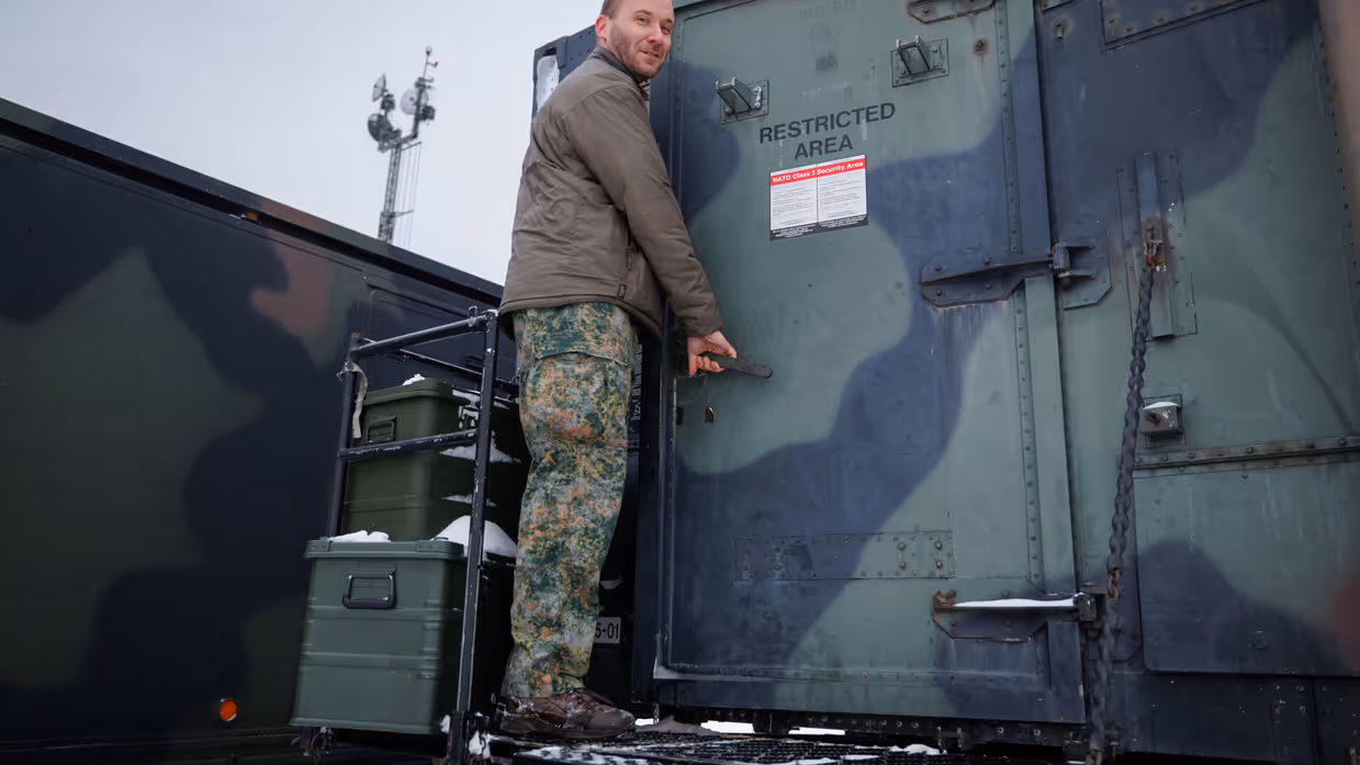 Op de linkerfoto opent luitenant Leon een deur van een groene werkcontainer. Op de rechterfoto is een Patriot-lanceerinrichting te zien door het prikkeldraad heen.