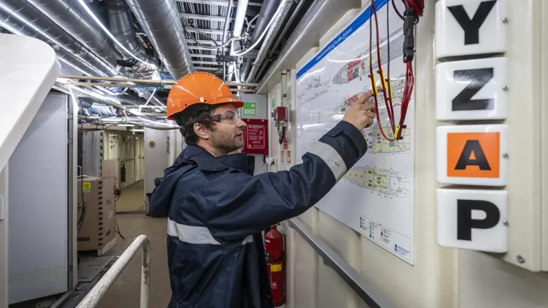 Alt-tekst: Jorren Stierman, senior-engineer Scheepsbouw, bekijkt aan boord van Zr.Ms. Holland een schematische tekening tijdens onderhoudswerkzaamheden.