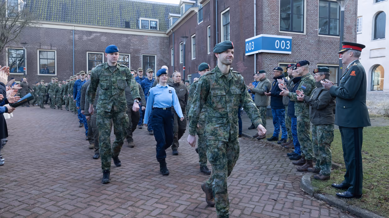  links: de staatssecretaris zit op een stoel. Rechts: Militairen lopen langs andere militairen