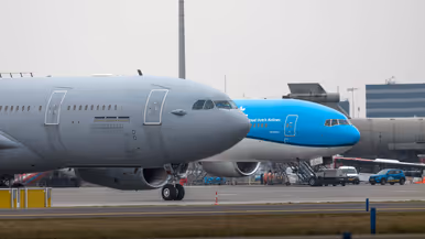 et geparkeerde tank- en transportvliegtuig, met daarachter een geparkeerd passagiersvliegtuig van KLM, met de kenmerkende blauwe kleur. 