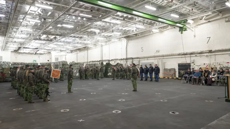 Alttekst: Militair personeel van de landmacht en marine staan in een hal tegenover elkaar opgesteld. 