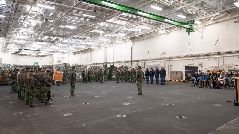 Alttekst: Militair personeel van de landmacht en marine staan in een hal tegenover elkaar opgesteld. 