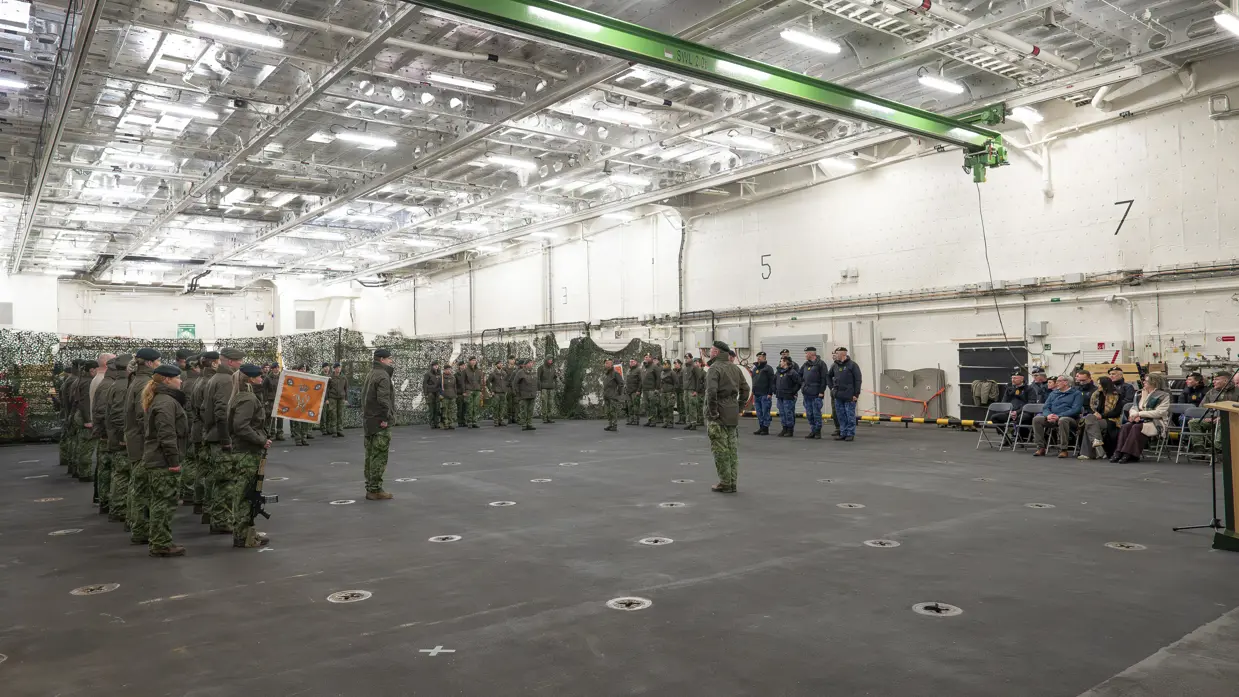 Alttekst: Militair personeel van de landmacht en marine staan in een hal tegenover elkaar opgesteld. 
