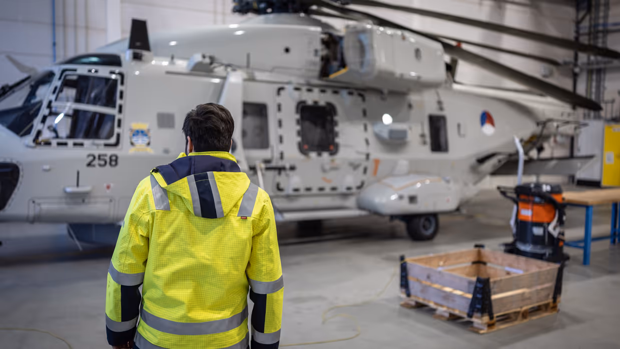 Een NH90 in de hanger met een medewerker van 990 Squadron op de voorgrond.  