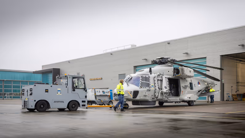 Een NH90 wordt door een tractor uit de hangar getrokken.  
