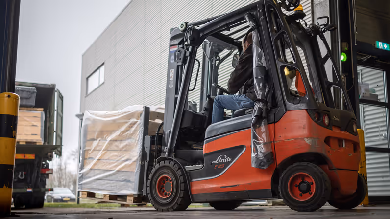 Een pallet wordt met een vorkheftruck in een groene vrachtwagen vanaf de zijkant ingeladen.