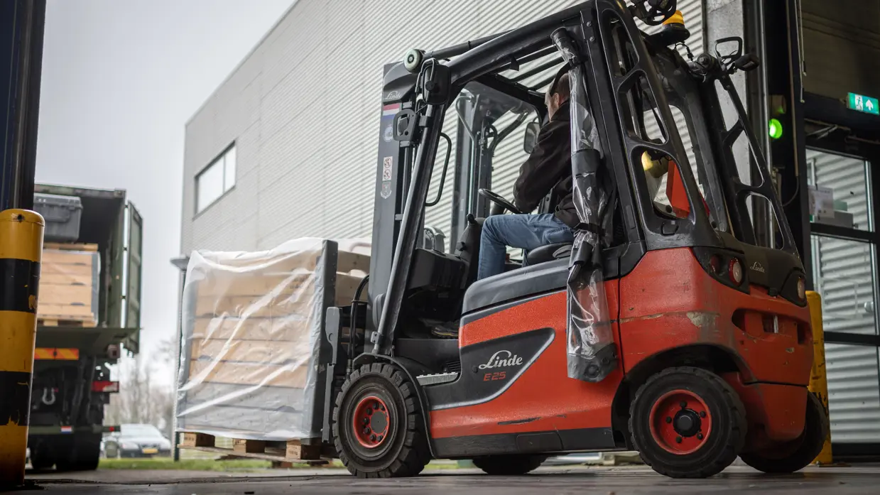 Een pallet wordt met een vorkheftruck in een groene vrachtwagen vanaf de zijkant ingeladen.