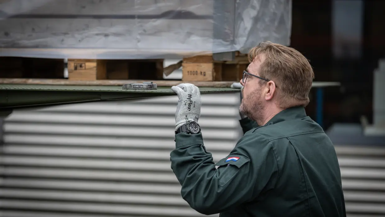Een medewerker monitort van dichtbij hoe een pallet wordt uitgeladen. Op de tweede foto een medewerker, gezeten achter zijn bureau.