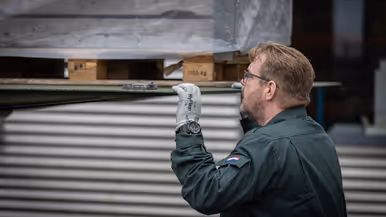 Een medewerker monitort van dichtbij hoe een pallet wordt uitgeladen. Op de tweede foto een medewerker, gezeten achter zijn bureau.