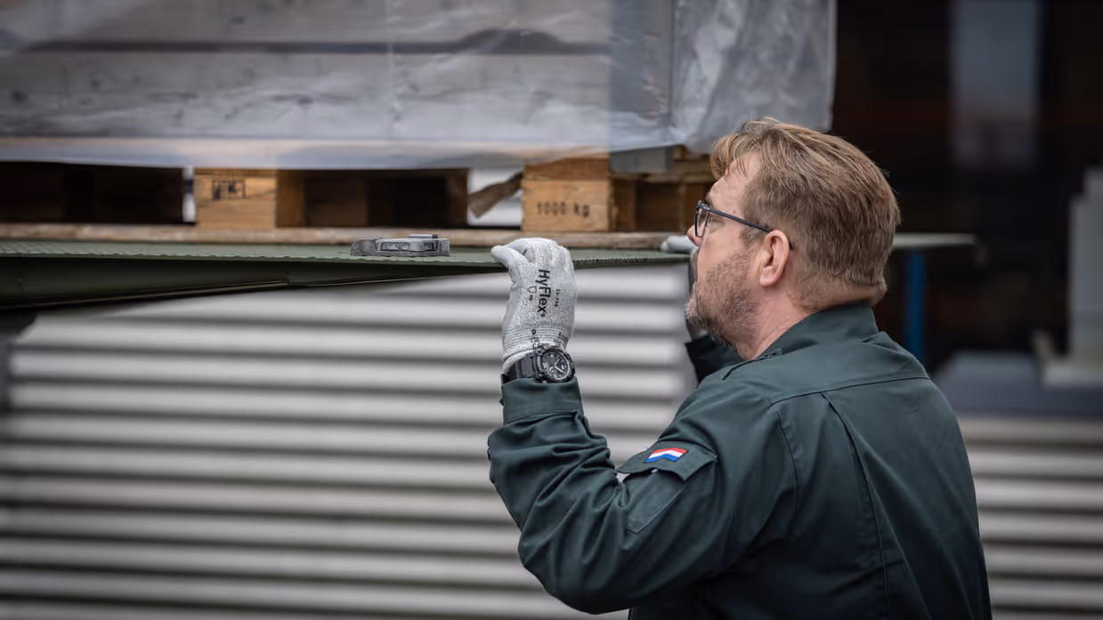 Een medewerker monitort van dichtbij hoe een pallet wordt uitgeladen. Op de tweede foto een medewerker, gezeten achter zijn bureau.