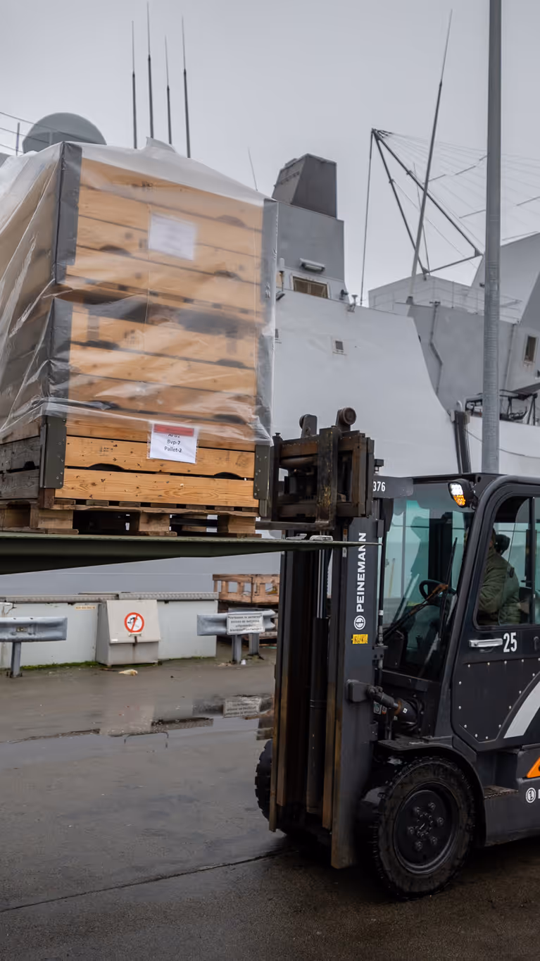 Een vorkheftruck die op de kade een pallet uit een vrachtwagen tilt.