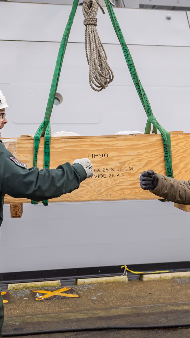 Twee collega’s geven elkaar een boks, met op de achtergrond een houten box, waarop NH90 staat.