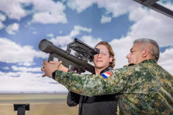 Staatssecretaris Tuinman kijkt door een vernieuwde Stinger-simulator. Aan de rechterkant een militair die de simulator vasthoudt.