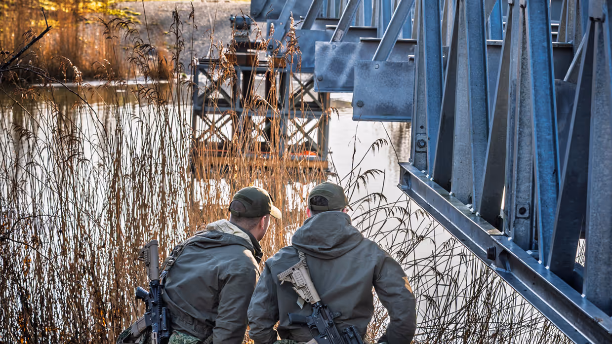 Twee militairen staan onder een deel van een brug. 