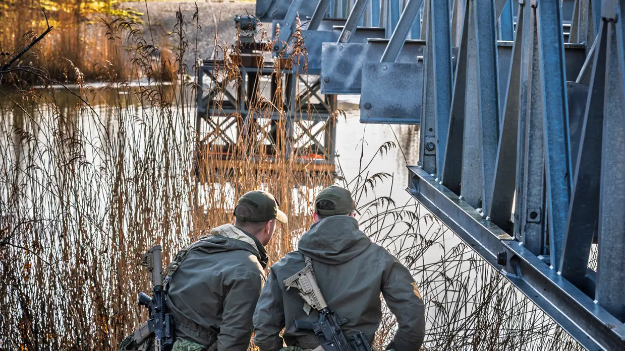 Twee militairen staan onder een deel van een brug. 