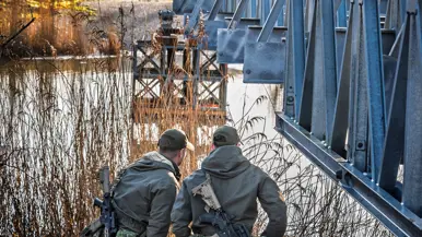 Twee militairen staan onder een deel van een brug. 