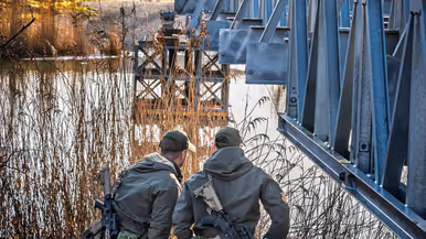 Twee militairen staan onder een deel van een brug. 