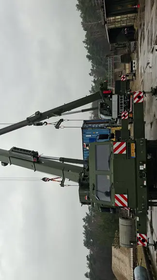 Twee hijskranen naast elkaar hijsen materialen op. 