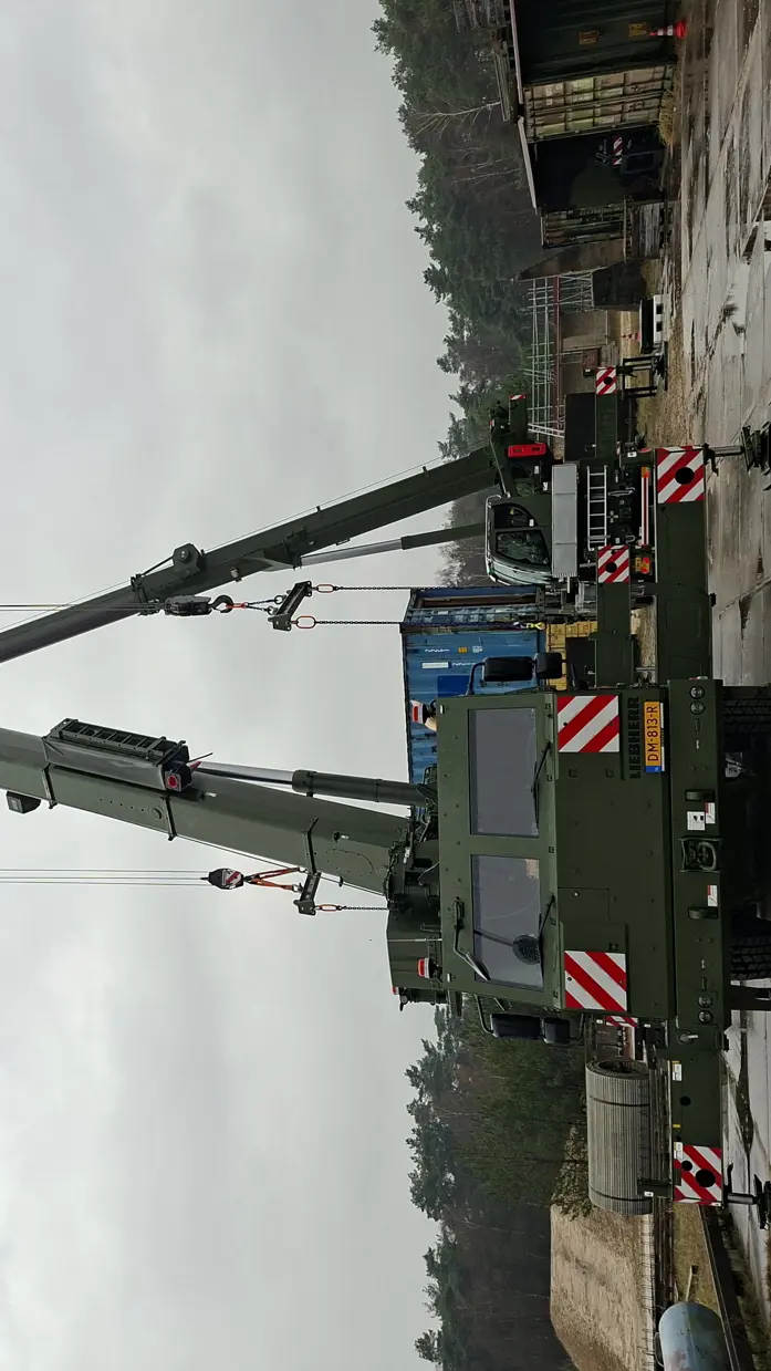 Twee hijskranen naast elkaar hijsen materialen op. 