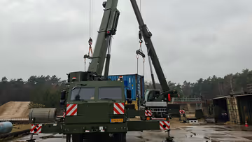 Twee hijskranen naast elkaar hijsen materialen op. 