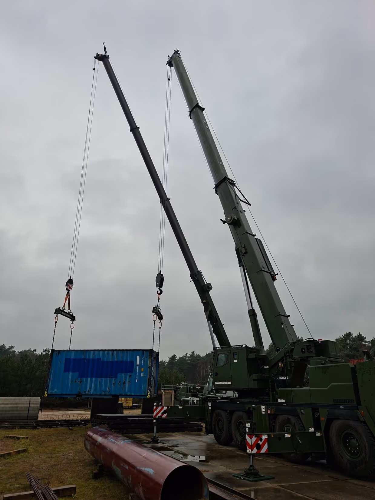 Twee hijskranen naast elkaar hijsen materialen op. 