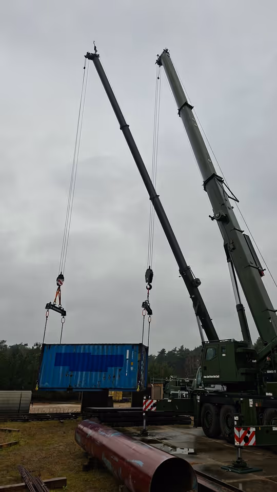 Twee hijskranen naast elkaar hijsen materialen op. 