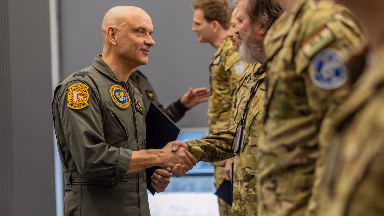 Luitenant-generaal Steur schudt de handen van de, onscherp in beeld gebrachte, vliegers.