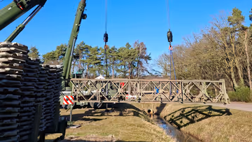 Twee hijskranen naast elkaar hijsen materialen op. 