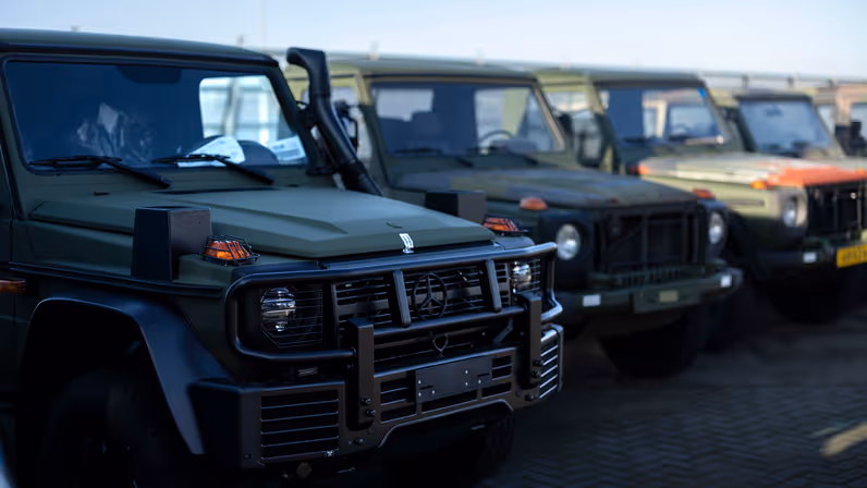 Een zijaanzicht van een Wolf GWT op de voorgrond en daarachter een rijtje verouderde MB’s. 