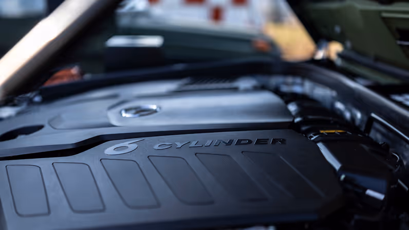 Het zijaanzicht van de motor met daarop een kunststof zwart dek, waarop ‘6 Cylinder’ staat.