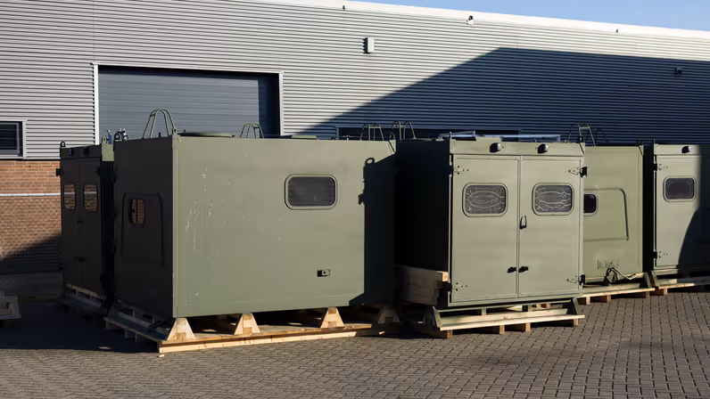 Een aantal groengespoten koffers die buiten de werkplaats wachten op montage.    