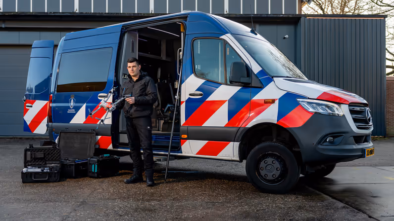 Adjudant Allard staat voor de dienstbus met een drone in zijn handen.