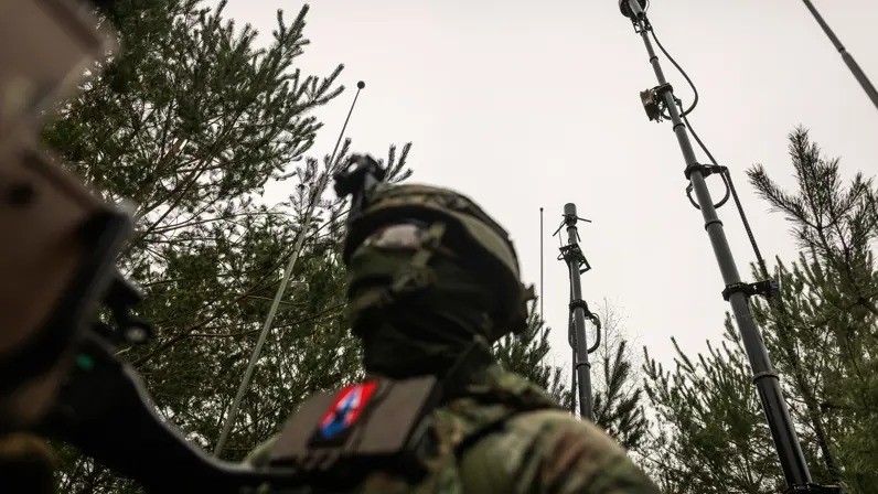 Een gecamoufleerde militair torent boven de gepantserde pantserwielvoertuig Boxer uit. Boven hen zijn diverse antennes te zien.