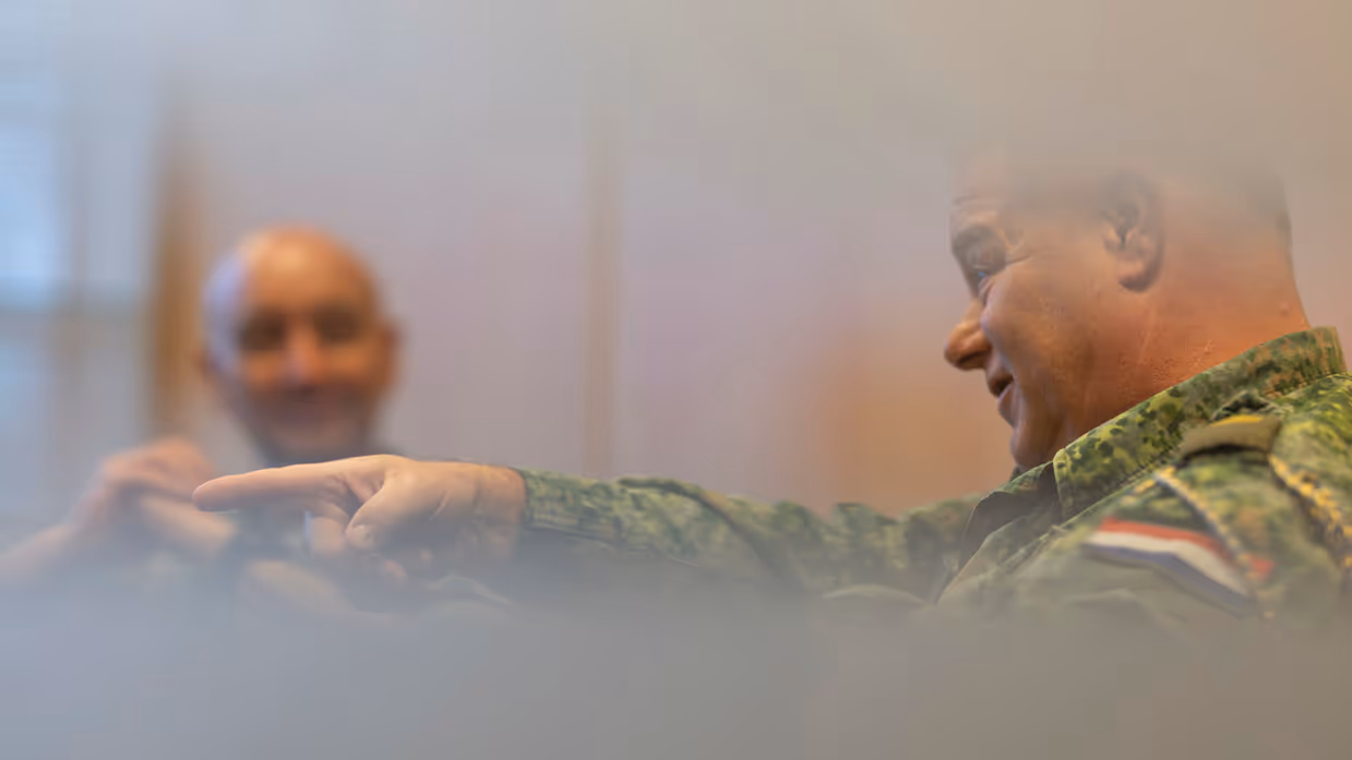 Oud-Luchtmachtadjudant Terry Venhovens spreekt geanimeerd en wijst met zijn wijsvinger. De nieuwe Luchtmachtadjudant Johan de Rooij kijkt Venhovens op de achtergrond aan.    