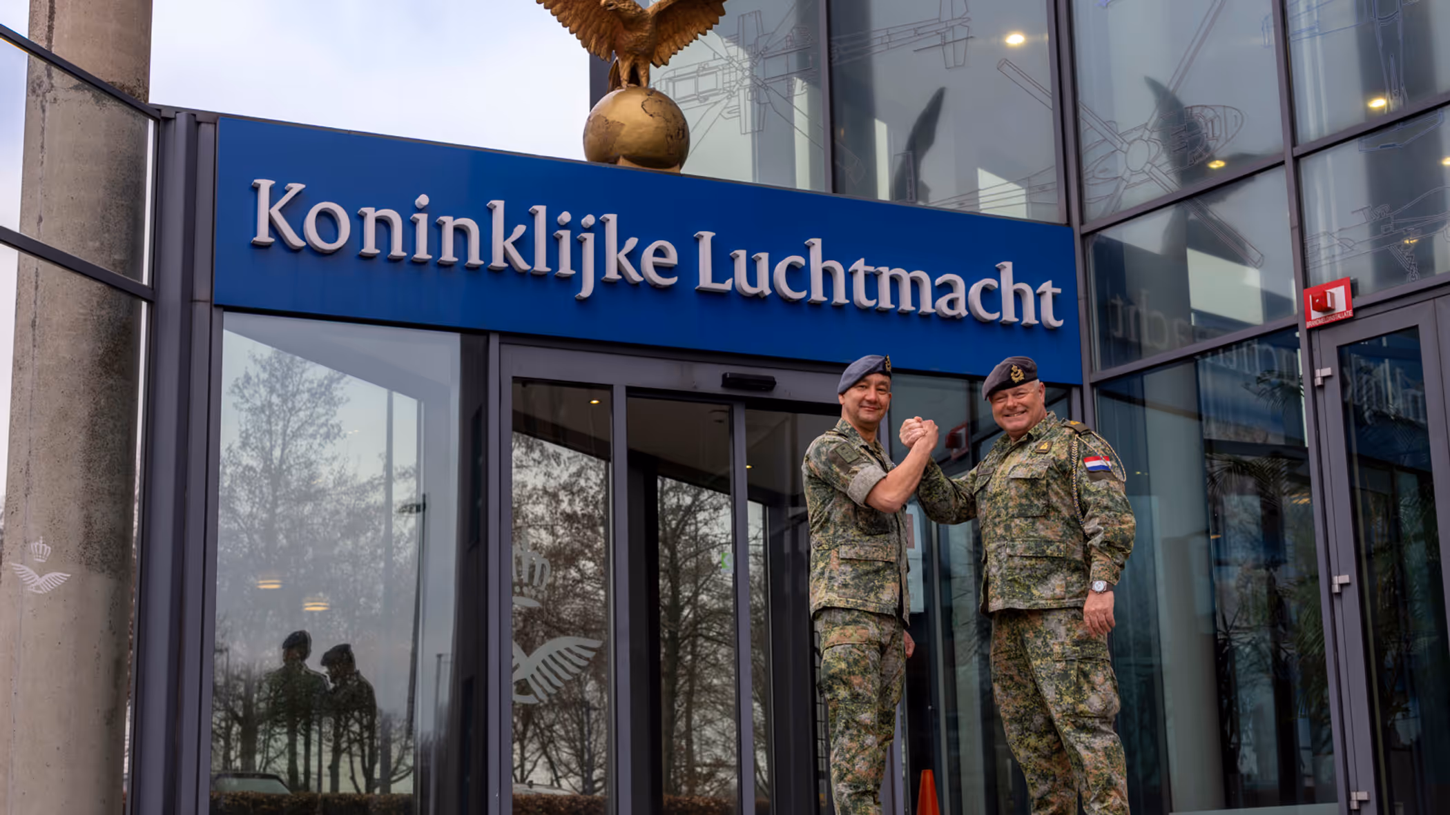  Luchtmachtadjudanten Terry Venhovens en Johan de Rooij schudden elkaar de hand voor de ingang van de Luchtmachttoren in Breda.