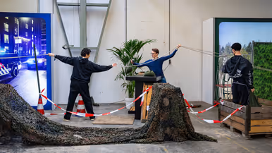 Diverse beelden van de fysieke uitdagingen, van links naar rechts: een team loopt met de handen aan een touw, waarbij ze over hindernissen moeten komen. Een team is gemaskerd en moet een ei in een dop over een parcours leiden. Rechts hangen twee deelnemers aan een rekstok.