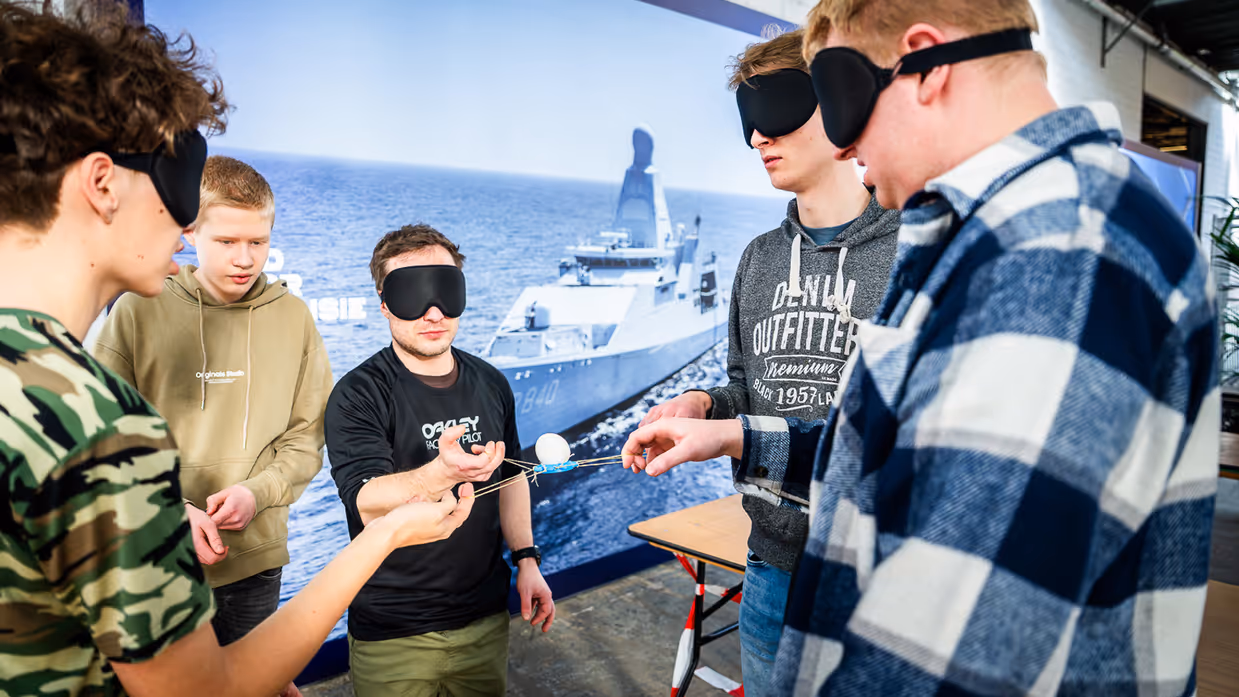 Diverse beelden van de fysieke uitdagingen, van links naar rechts: een team loopt met de handen aan een touw, waarbij ze over hindernissen moeten komen. Een team is gemaskerd en moet een ei in een dop over een parcours leiden. Rechts hangen twee deelnemers aan een rekstok.