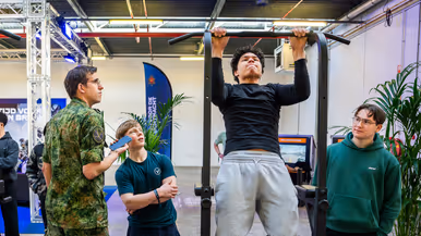 Diverse beelden van de fysieke uitdagingen, van links naar rechts: een team loopt met de handen aan een touw, waarbij ze over hindernissen moeten komen. Een team is gemaskerd en moet een ei in een dop over een parcours leiden. Rechts hangen twee deelnemers aan een rekstok.