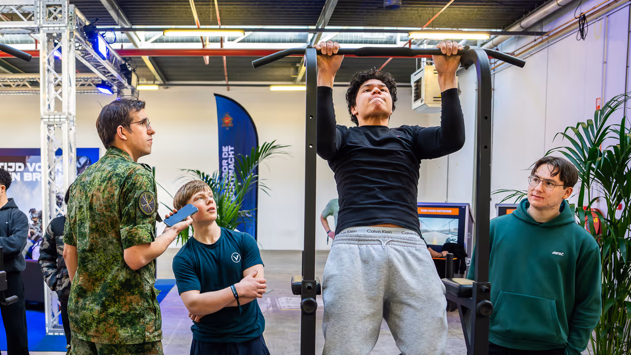 Diverse beelden van de fysieke uitdagingen, van links naar rechts: een team loopt met de handen aan een touw, waarbij ze over hindernissen moeten komen. Een team is gemaskerd en moet een ei in een dop over een parcours leiden. Rechts hangen twee deelnemers aan een rekstok.