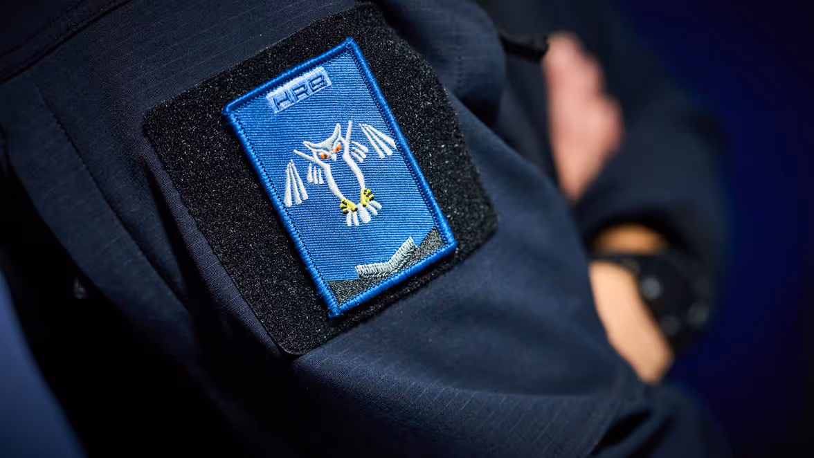 Een onherkenbaar persoon zit achter 3 computerschermen terwijl hij op het toetenbord tikt. 