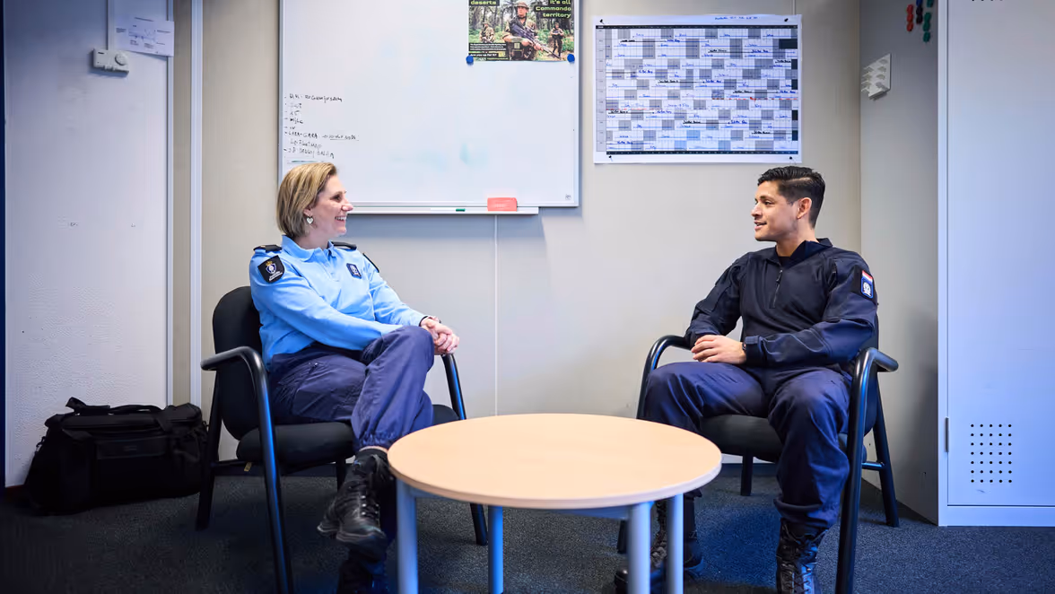 Adjudant Carolien en kapitein Tobias zitten tegenover elkaar in stoelen en praten lachend met elkaar.