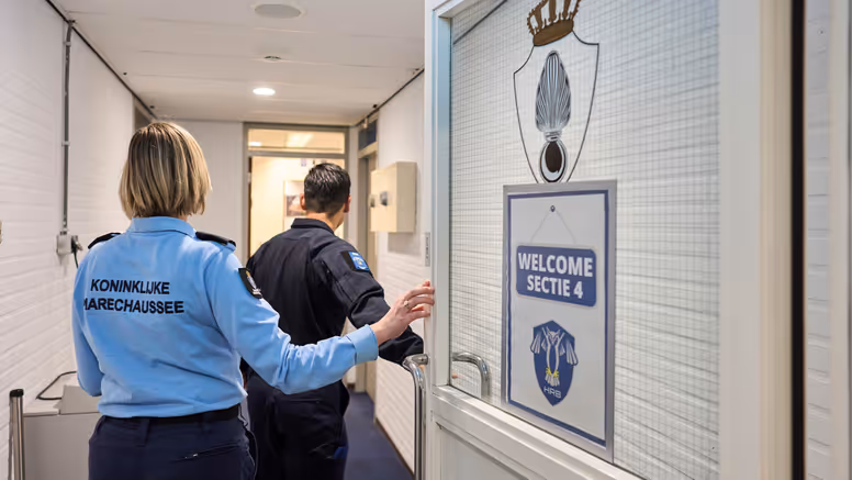 Adjudant Carolien en kapitein Tobias stappen door een deur waarop ‘Welcome Sectie 4’ wordt afgebeeld.
