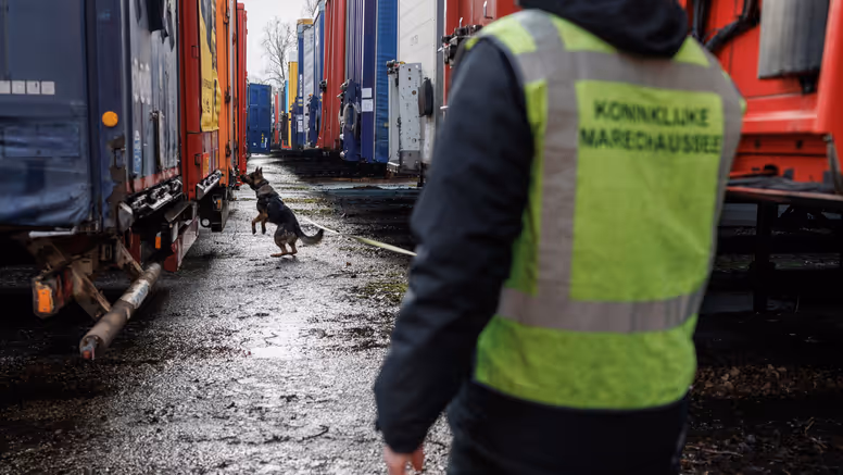 Een aangelijnde diensthond van de KMar snuffelt aan een van de vele trailers.