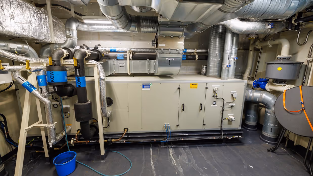 Een ruimte aan boord met daarin verschillende witte kasten en afzuiginstallaties.